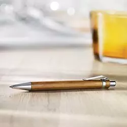 Penna bamboo personalizzata su scrivania in legno con bicchiere sullo sfondo