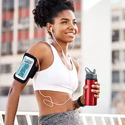 borracce-alluminio personalizzata adatte per lo sport ragazza che fa sport appoggiata su una ringhiera o muro con porta telefono da braccio e auricolari per ascoltare la musica