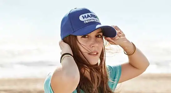 cappelli personalizzati con visiera indossato da ragazza in spiaggia con occhiali da sole