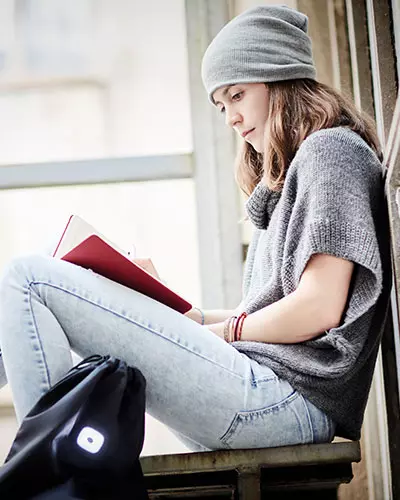 cappello personalizzato grigio cuffia inverale indossato da ragazza seduta sulle scale che legge un libro 