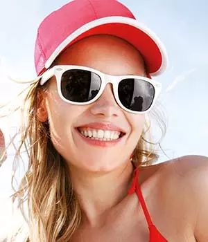 occhiali da sole personalizzati indossati da ragazza bionda in spiaggia con cappellino da baseball