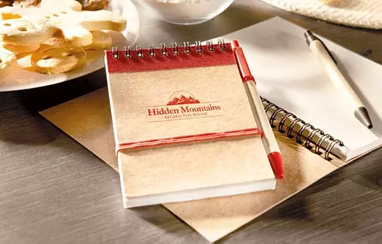 quaderno personalizzabile e penna corredata in cartone ecologico appoggiato su tavolo per colazione