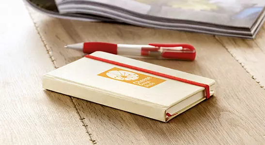 quaderno con elastico e penna corredata in cartone ecologico appoggiato su tavolo per colazione