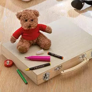 set di matite in elegante valigetta regalo appoggiata su tavolo in legno con orsacchiotto di peluche che indossa maglietta rossa