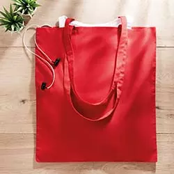 Shopper cotone rossa posata su scrivania in legno con cuffiette che escono dal suo interno