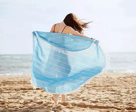telo mare personalizzato azzurro a fighe bianche con frange indossato da ragazza in spiaggia 